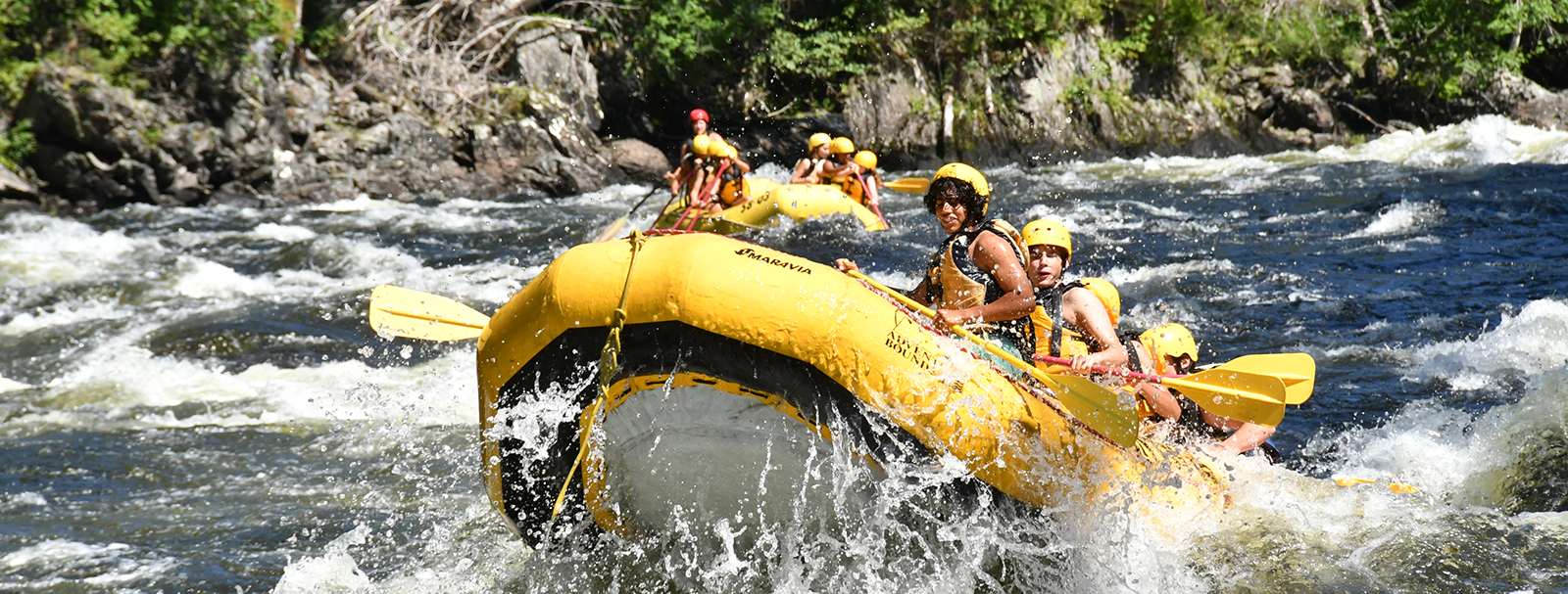 Kids whitewater rafting on the Kennebec river, yellow raft splashing into waves.